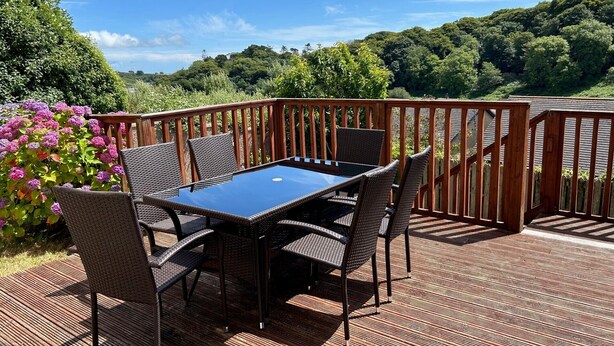 A deck with a table and chairs, surrounded by a wooden railing, overlooking a lush green landscape. - Glen Ard Holiday Home no. 1 (Dunmore East)