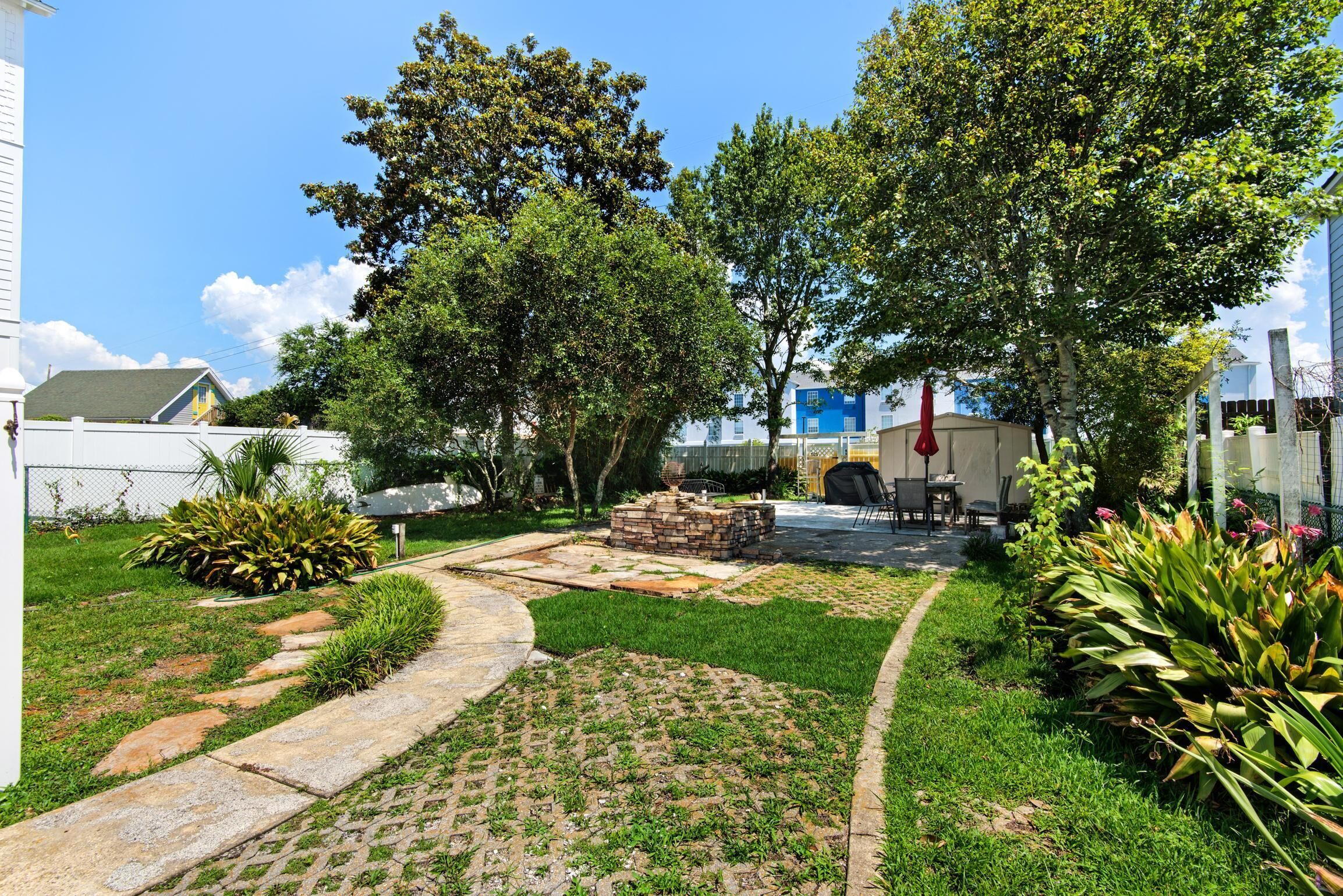 A well-maintained garden with a paved pathway, a stone fire pit, and various plants.