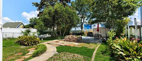 A well-maintained garden with a paved pathway, a stone fire pit, and various plants.