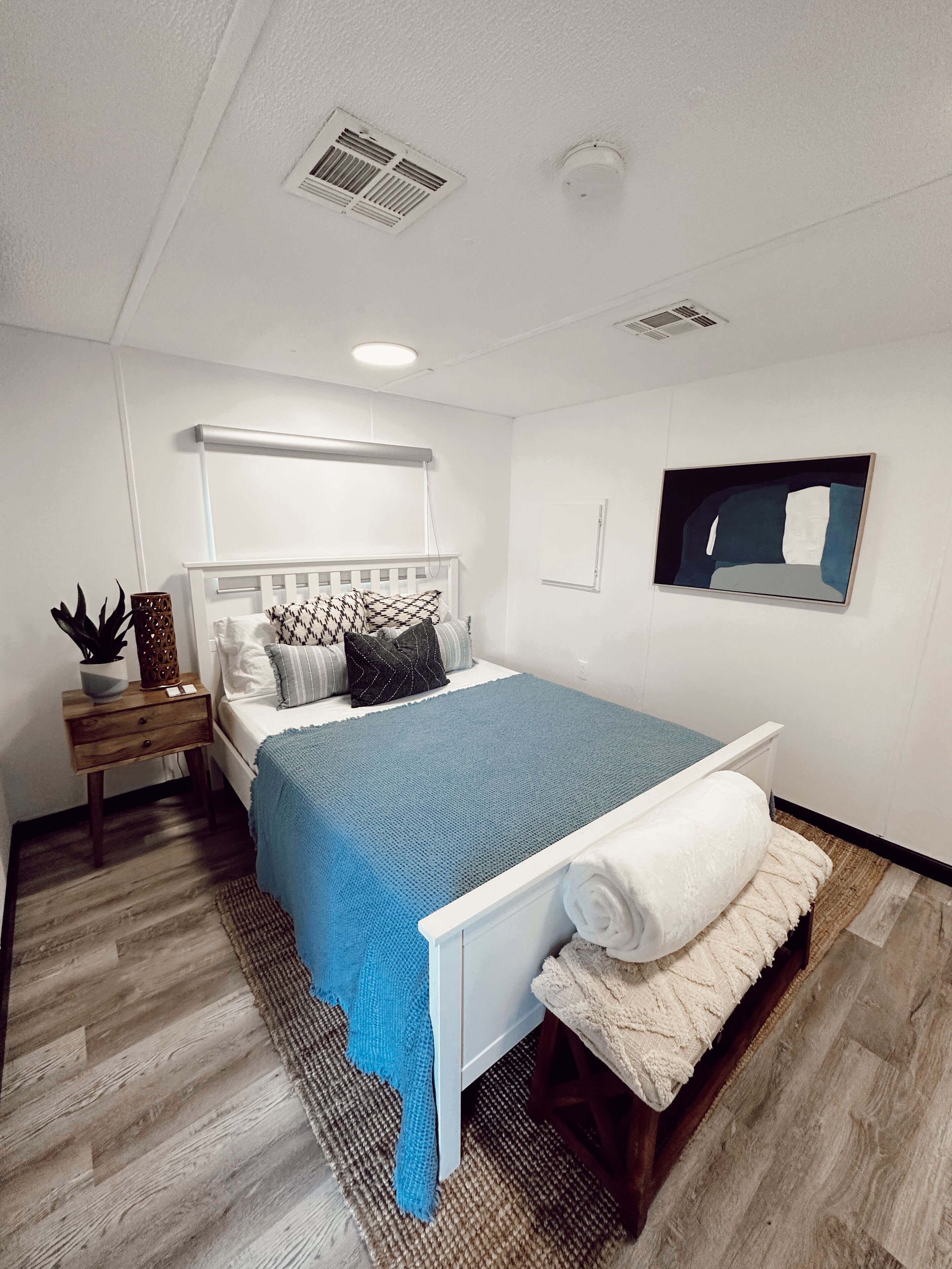 Een moderne slaapkamer met een bed, nachtkastjes, een spiegel en een ventilatie rooster.