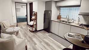 Eine moderne Küche mit Kühlschrank, Spüle und Holzschränken. Es gibt einen Essbereich mit Tisch und Stühlen sowie ein Wohnzimmer mit Sofa und Couchtisch.