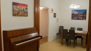 Et værelse med et træpiano, et spisebord med stole og to billeder på væggene.