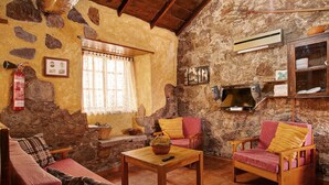 A rustic living room with stone walls, a wooden ceiling, a fireplace, a sofa, two armchairs, and a coffee table.