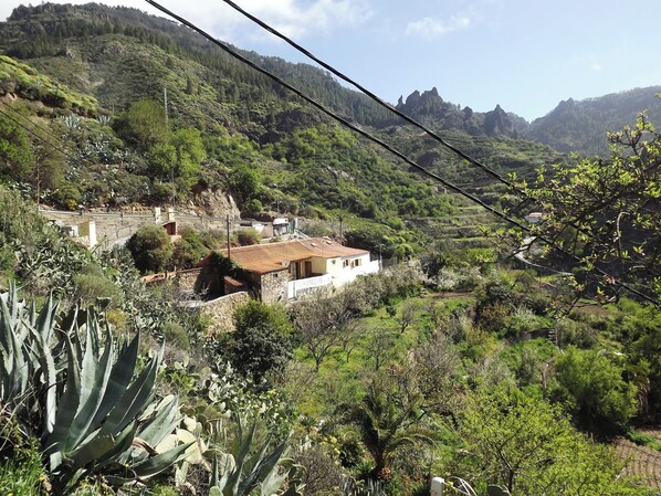 A rural landscape with a white building with a red roof, surrounded by greenery and hills. - House Sleeps6-parking-garden-pool in Summer-pet (Tejeda)