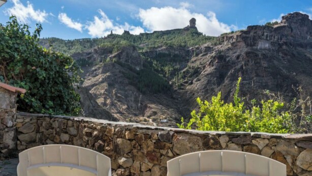A stone wall with two beige chairs facing a mountainous landscape.