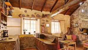 A rustic kitchen with stone walls, wooden beams, a built-in bar, and a stone sink.