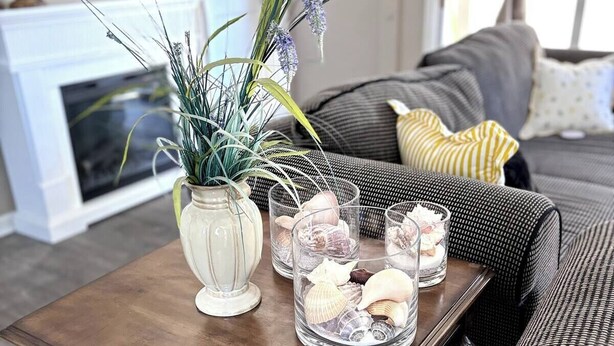 Una mesa de centro de madera con un florero y frascos de vidrio con caracolas.