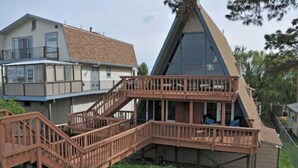 Una pequeña cabaña de techo a dos aguas con terraza de madera y escaleras que suben a un balcón.