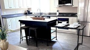 Una cocina moderna con armarios blancos, un refrigerador de acero inoxidable y una mesa de comedor de madera con sillas.