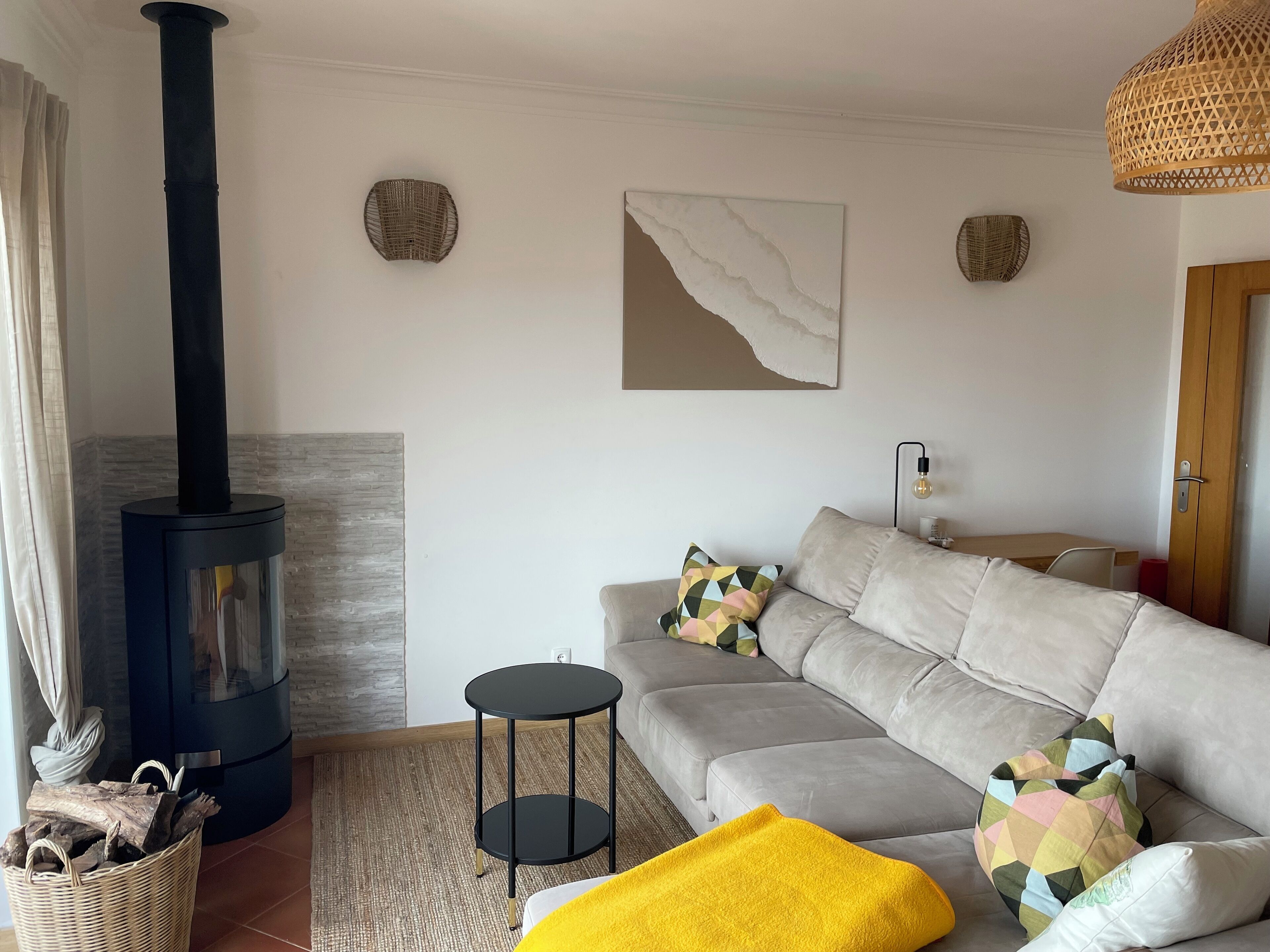 Ein Wohnzimmer mit einer Couch, einem kleinen Beistelltisch, einem schwarzen Kamin und einem gewebten Korb auf dem Boden.