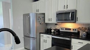 A modern kitchen with white cabinets, stainless steel appliances, and a black countertop. - The Dreamy Dwelling (Pooler)