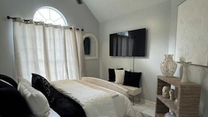A bedroom with a bed, a ceiling fan, a TV, and a window with curtains. - The Dreamy Dwelling (Pooler)