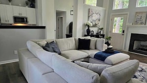 A modern living room with a sectional sofa, a fireplace, and a kitchen area in the background. - The Dreamy Dwelling (Pooler)
