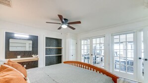 Ein Schlafzimmer mit Bett, Deckenventilator, Fenster mit Aussicht und einer Tür zum Balkon.