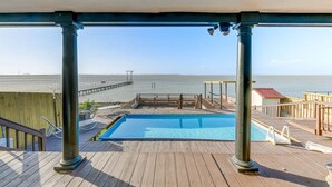 Eine Holzterrasse mit Pool, mit Blick auf einen Strand und einen Steg.