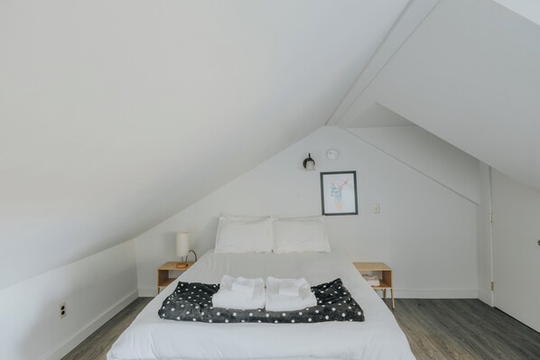 A bedroom with a bed, a bedside table, a nightstand, a wall-mounted lamp, and a framed picture.