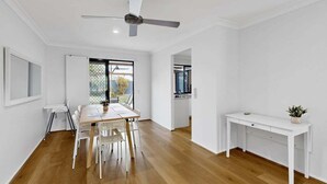 Une pièce spacieuse avec un plancher en bois, une table à manger avec des chaises, un bureau blanc et un ventilateur de plafond.