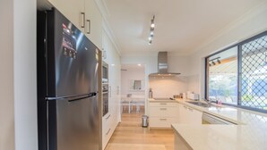Une cuisine moderne dotée d’un réfrigérateur en acier inoxydable, de meubles blancs, d’un plancher en bois et d’une grande fenêtre offrant une belle vue.