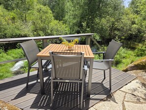 Une terrasse en bois avec une table et des chaises, offrant une vue sur un paysage naturel composé d’arbres et d’un ruisseau.