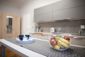 Et køkken med en frugtkurv på bordet, en bakke med kopper og en trædør i baggrunden.