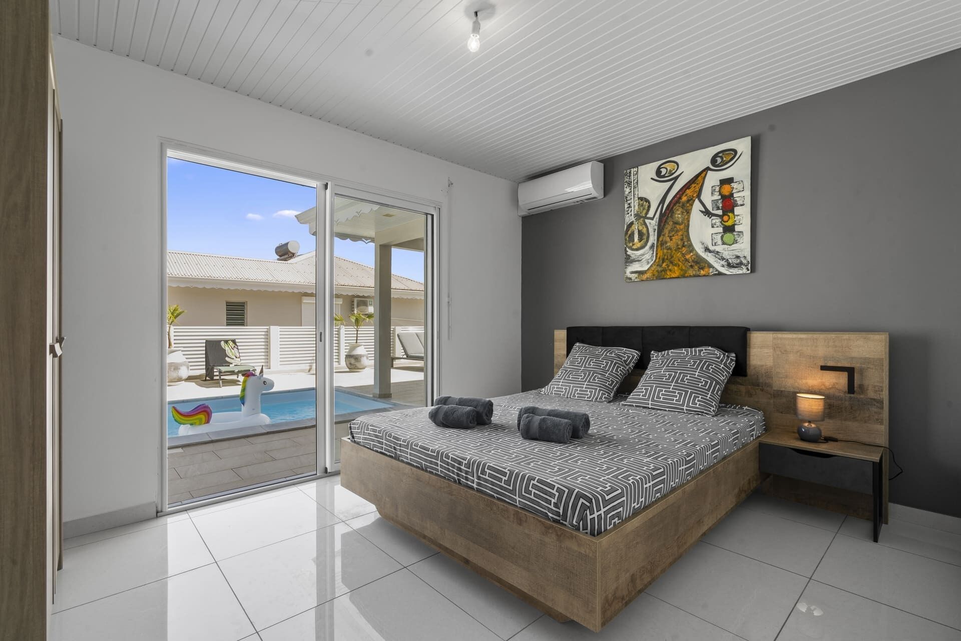A modern bedroom with a large bed, a nightstand, and a painting on the wall.