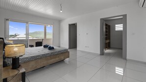 Quarto moderno com uma cama grande, mesa de cabeceira, luminária e vista para o exterior.