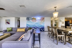 Una sala de estar moderna con un sofá gris, una mesa de comedor de madera y un mural con diseño de ola.