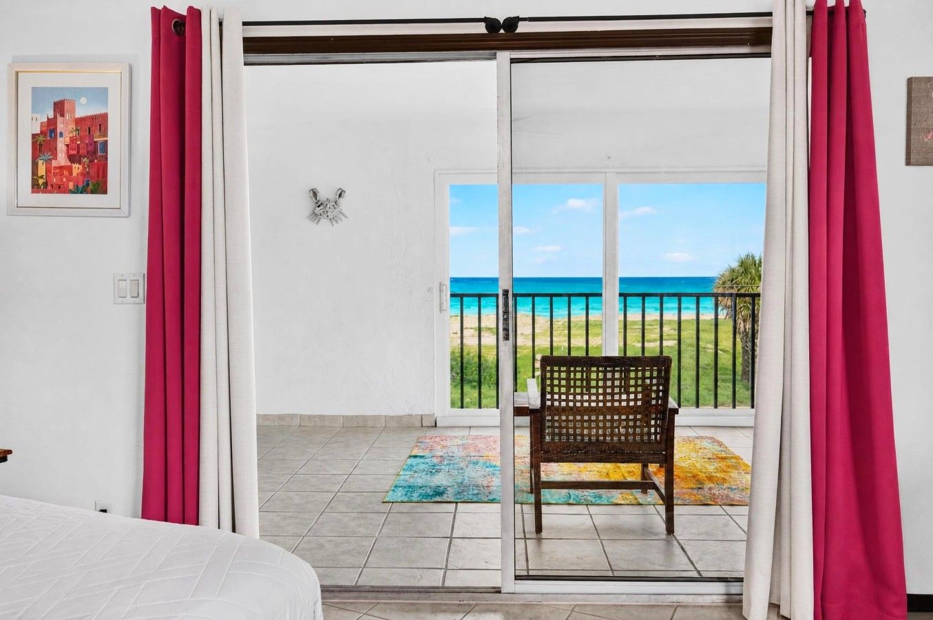 Ein Zimmer mit einem Bett, einer Sitzbank und Blick auf den Strand durch eine Glastür.
