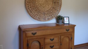 Un mueble de madera con tres cajones y dos puertas, una cesta tejida en la pared y una planta pequeña en maceta encima del mueble.
