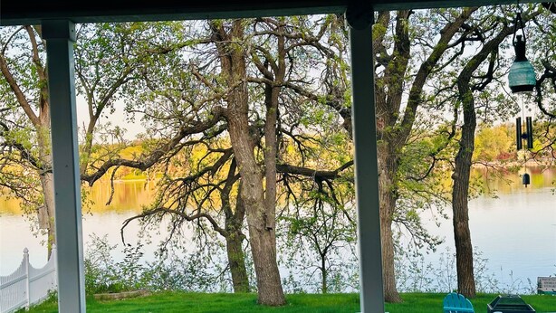 Vista al lago desde un balcón techado, con árboles y una señal al fondo.