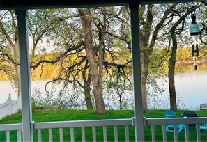 A lakeside view from a covered deck with trees and a sign in the background. - Charming 3-bedroom Legacy Lakehouse near Spicer with beautiful view of the lake! (Spicer)