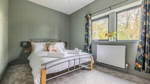 Ein Schlafzimmer mit Bett, einem Fenster mit Vorhängen, einem Heizkörper und Blick auf Bäume.
