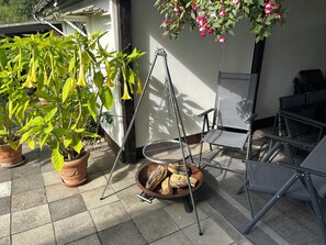 A patio with a metal chair, a hanging flower pot, and a fire pit with logs.