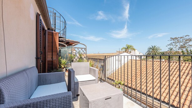 A balcony with wicker furniture, a metal railing, and a view of the cityscape.