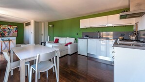 A modern kitchen with white cabinets, a dining area with a white table and chairs, and a green accent wall.