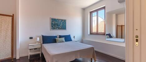 A bedroom with a bed, bedside tables, a window, and a painting on the wall.