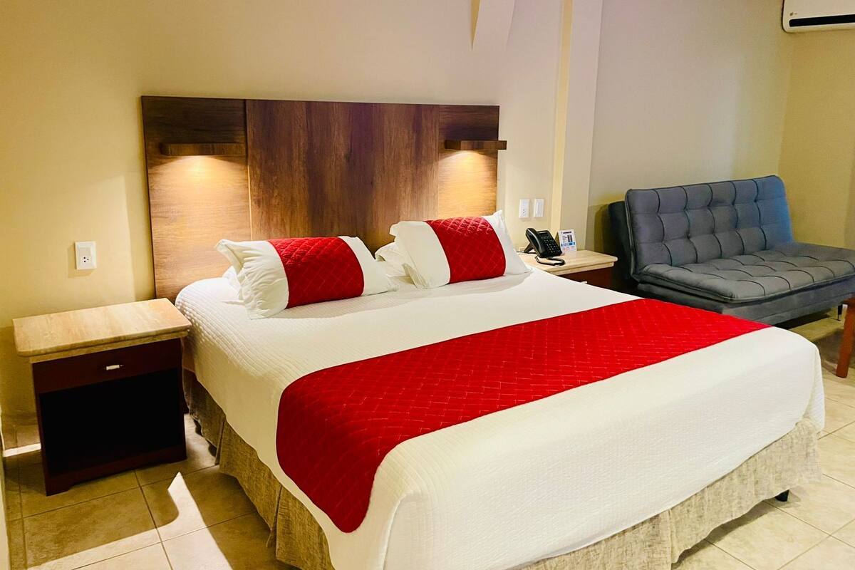 A hotel room with a large bed, a bedside table, a chair, and a wall-mounted phone.