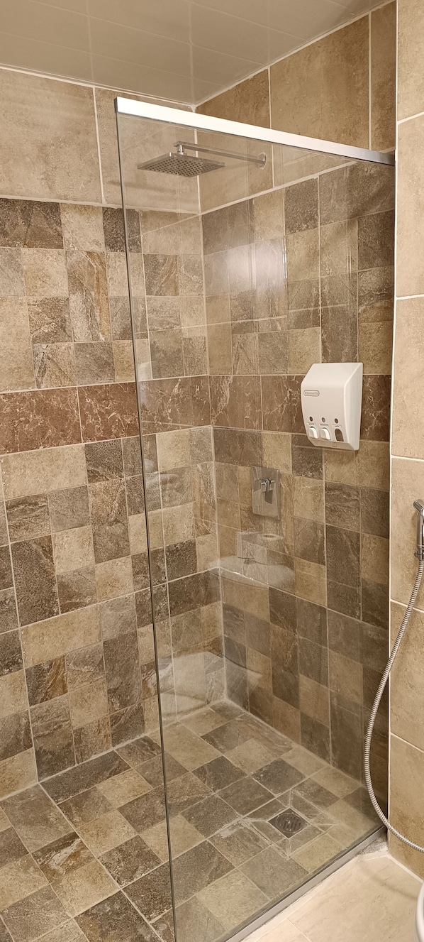 A shower with a glass door, tiled walls, and a handheld showerhead. - HOTEL LOS CEIBOS (Tarija)