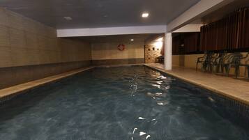 Una piscina interior con agua cristalina, paredes enlosadas y un flotador en la pared.