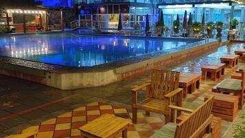 Un espace piscine doté d’une terrasse carrelée, de chaises et de tables en bois.
