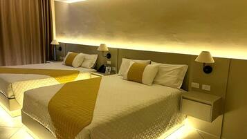 A hotel room with two beds, each with a headboard, bedside tables, lamps, and a curtain.