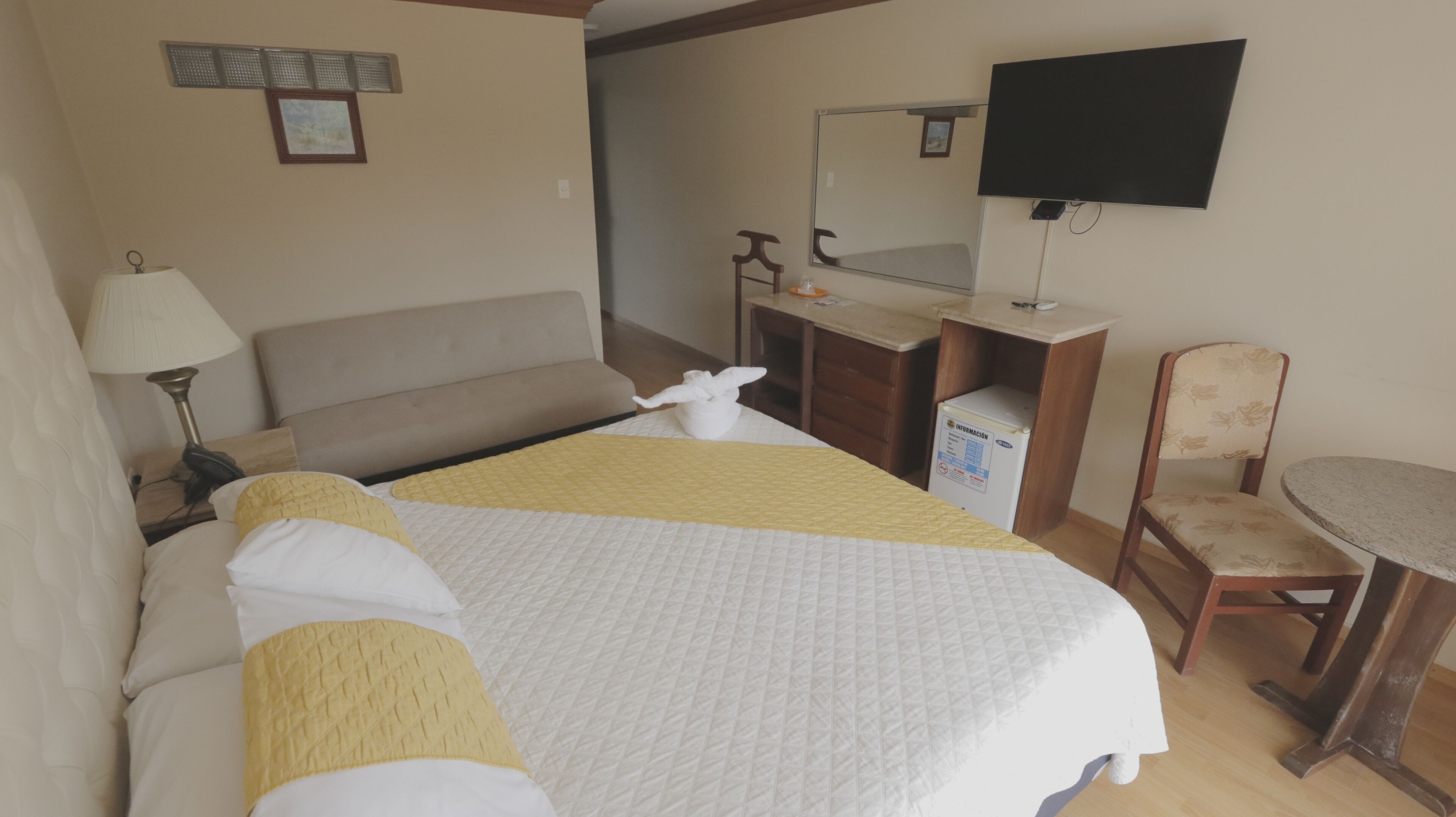 Une chambre d’hôtel équipée d’un lit, d’une table de chevet, d’une lampe, d’un bureau, d’une chaise et d’un téléviseur fixé au mur.