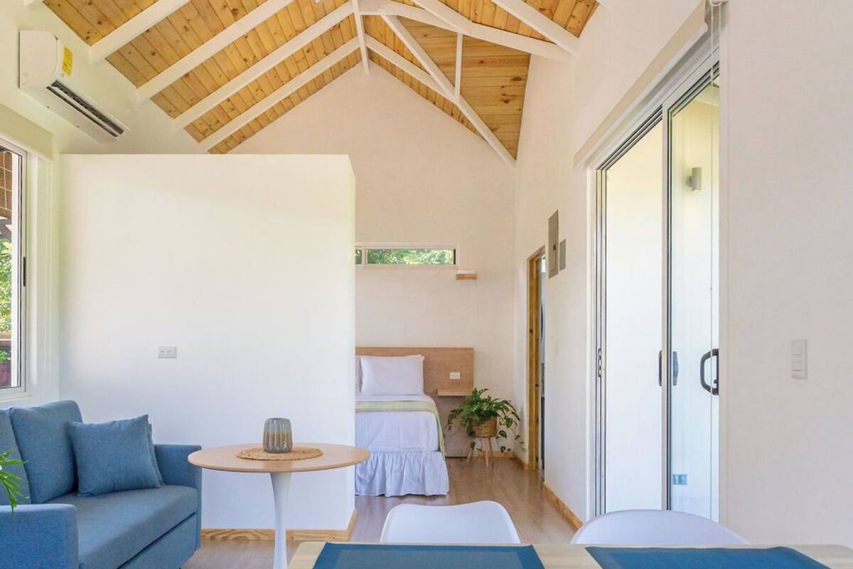 A modern room with a high wooden ceiling, a bed, a blue sofa, and a small table with a mat.