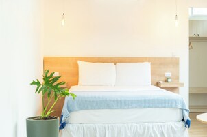 Un dormitorio ordenado con cama, mesita de noche y una planta en maceta.
