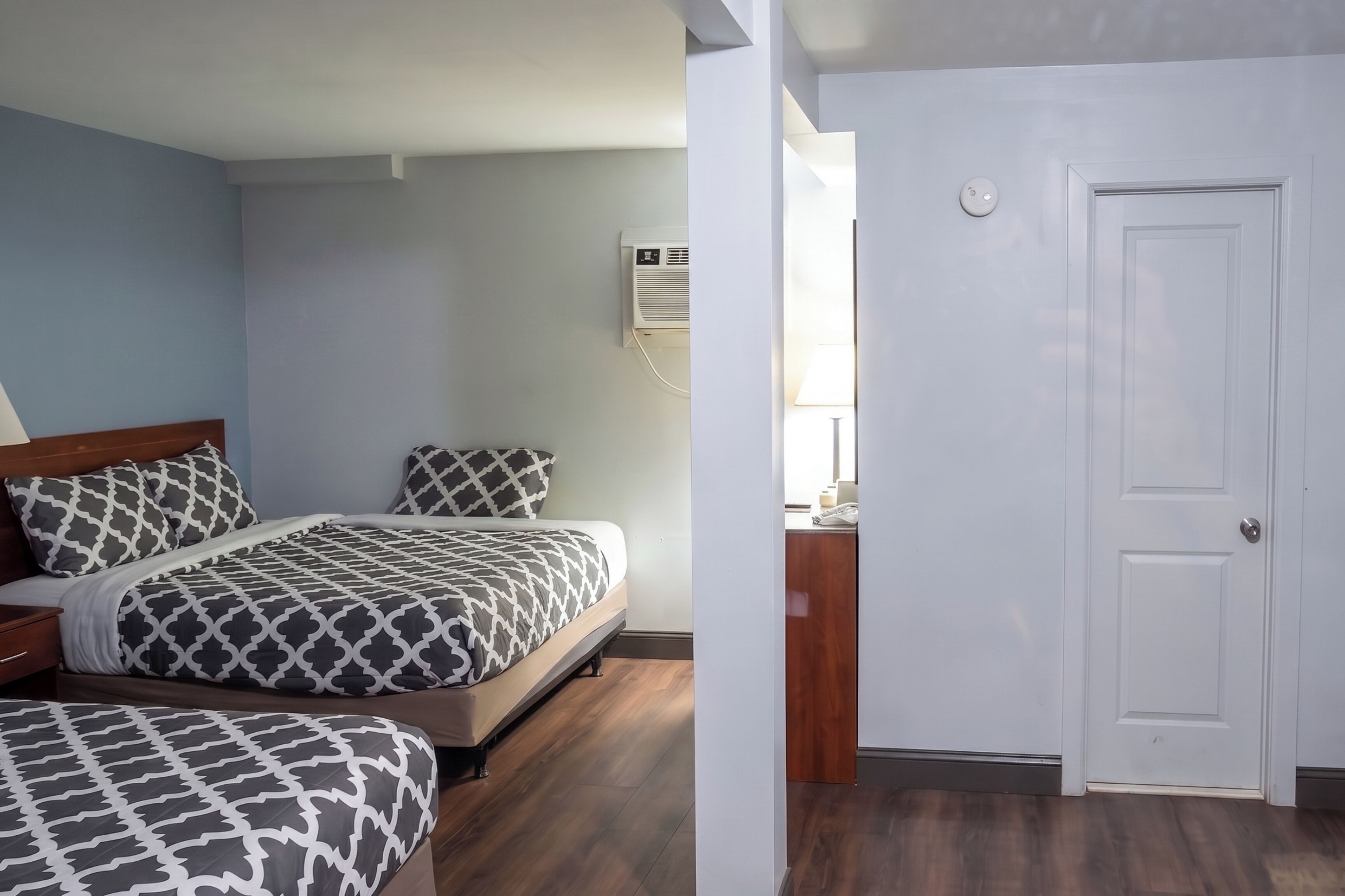 Een slaapkamer met twee bedden, een nachtkastje, een wandairconditioner en een deur.