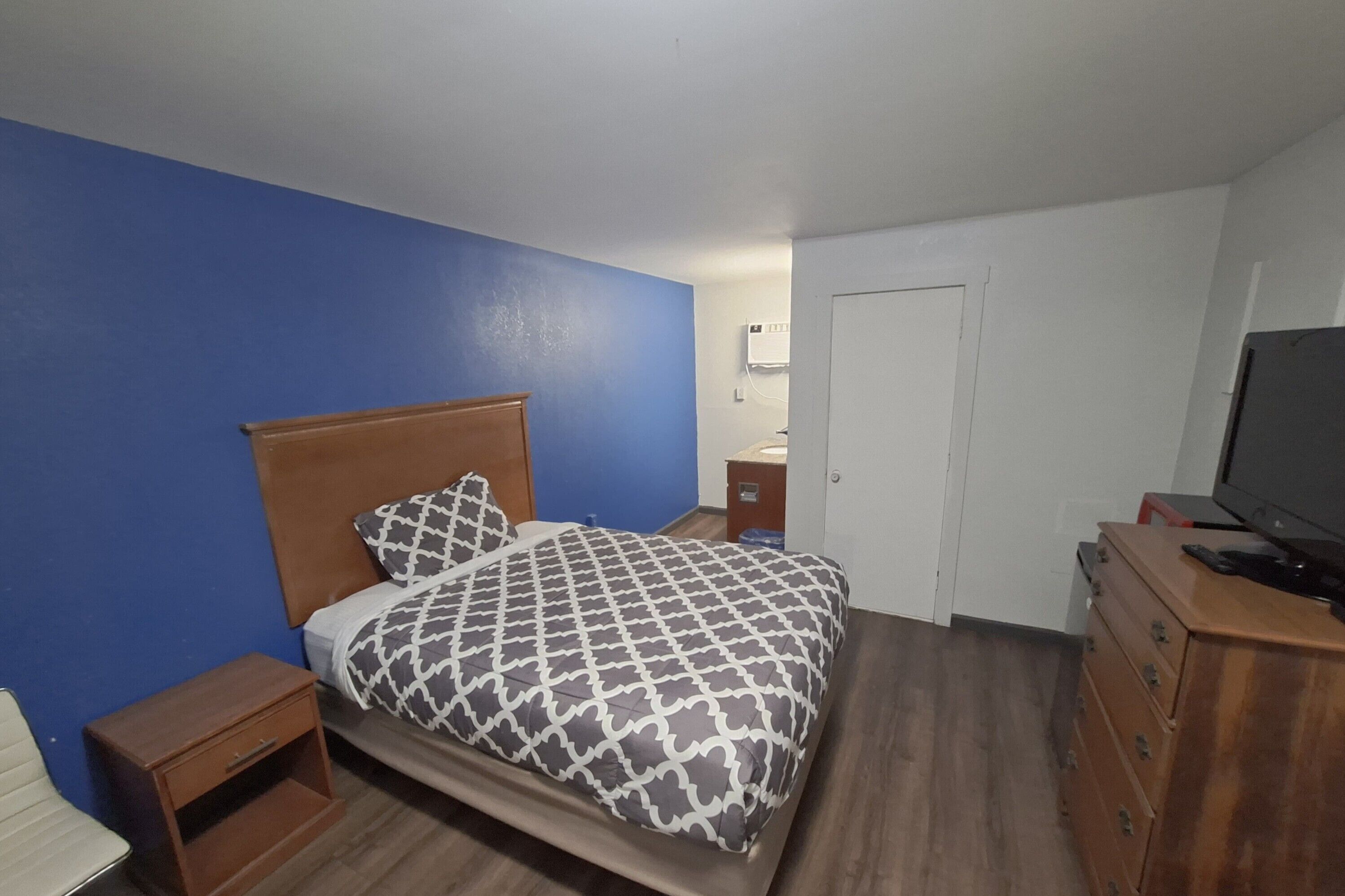 A bedroom with a bed, a wooden dresser, a television, and a white door.