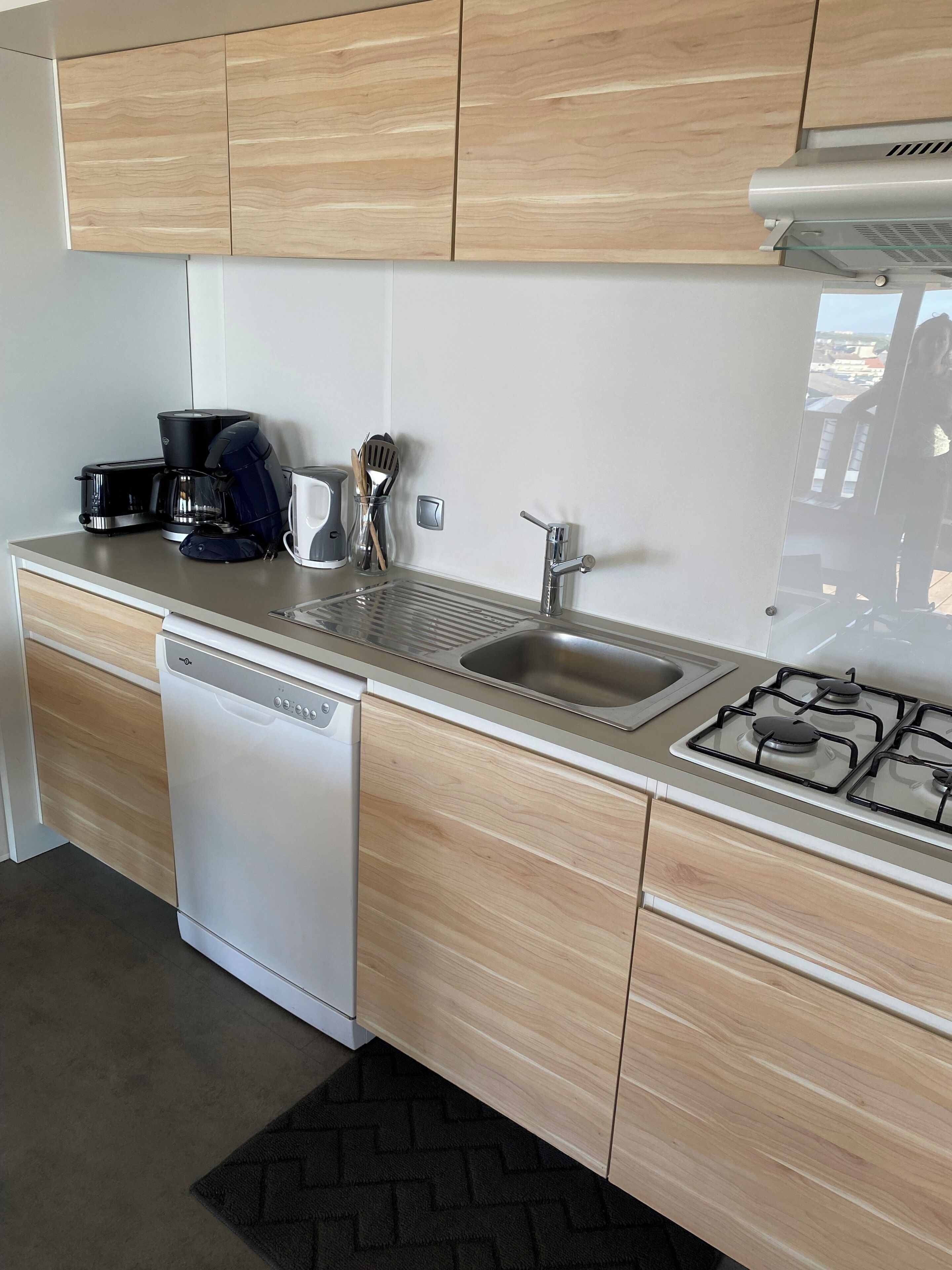Una cucina moderna con mobili in legno, lavastoviglie, piano cottura e macchina da caffè.