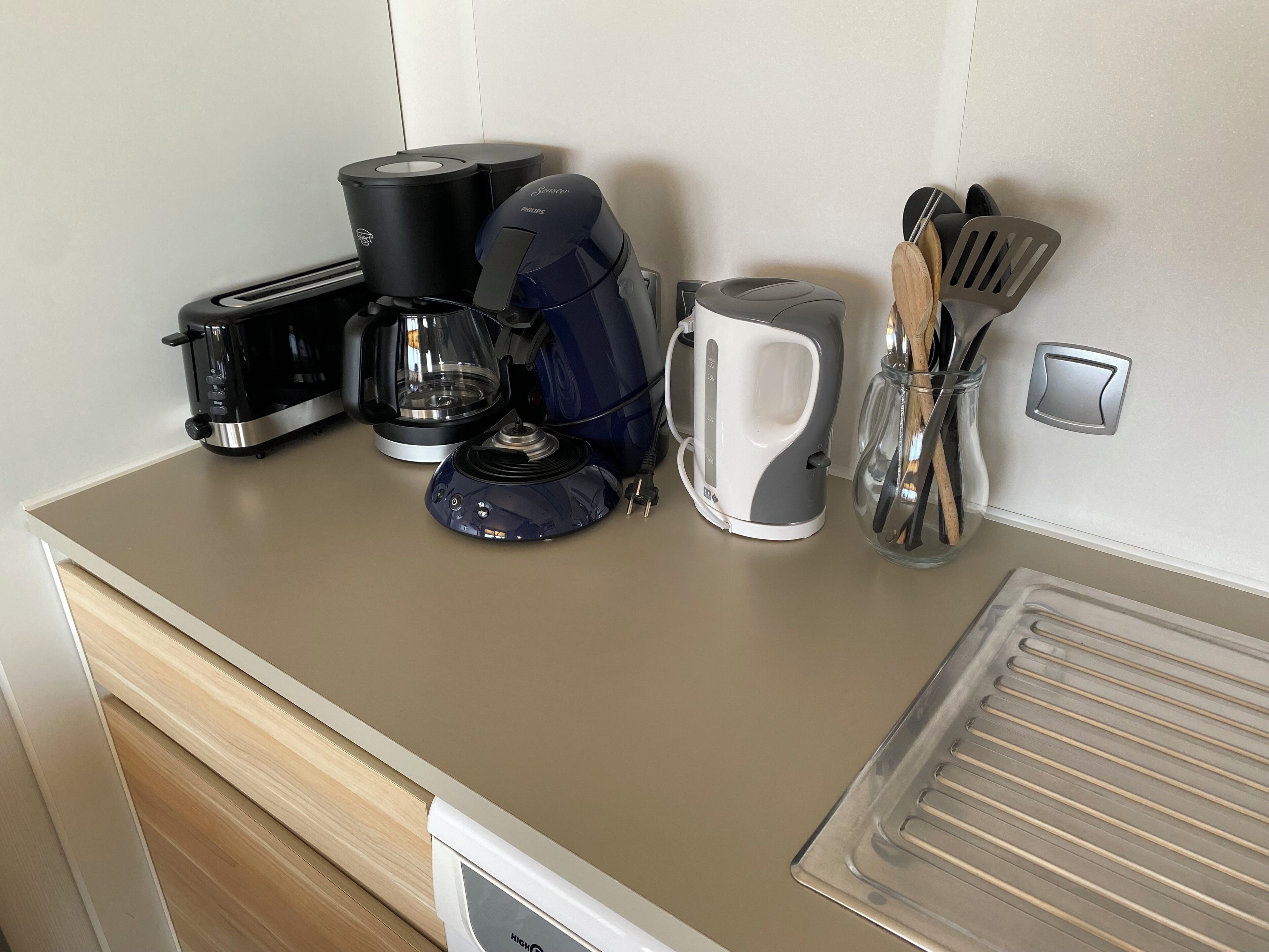 A kitchen counter with a coffee maker, toaster, kettle, and utensils.