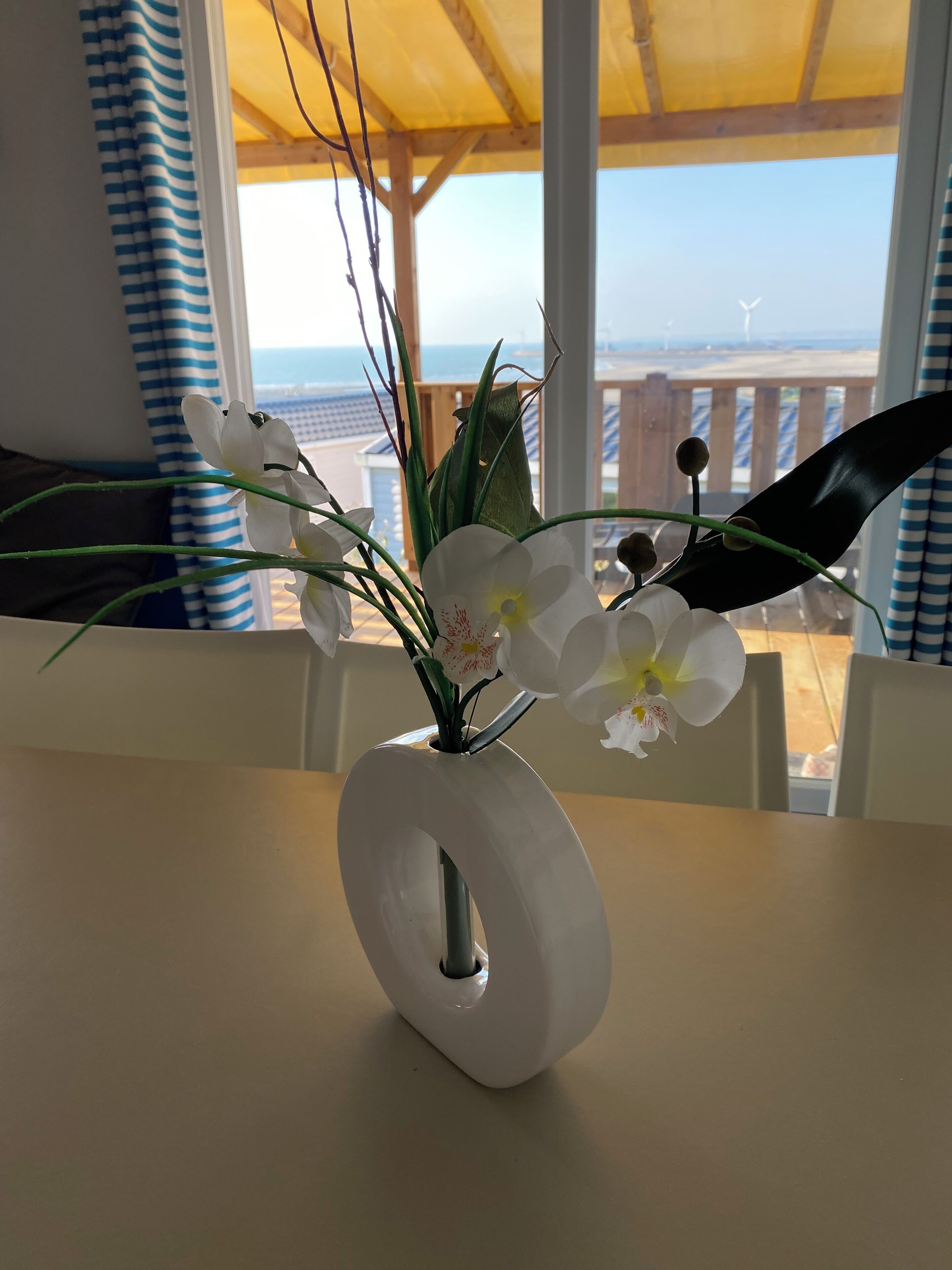 Un vase blanc à la forme originale, posé sur une table, et contenant des fleurs blanches dont le cœur est jaune.
