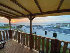Une terrasse en bois offrant une vue sur une plage et l’océan au coucher du soleil.